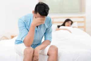 Man experiencing erectile dysfunction sitting on the edge of a bed, appearing concerned